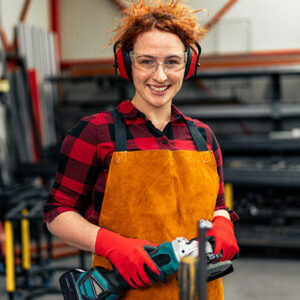 employée tenant dans sa main une meuleuse, elle est équipe d'un casque réducteur de bruit, de lunettes protectrices et de gants adaptés